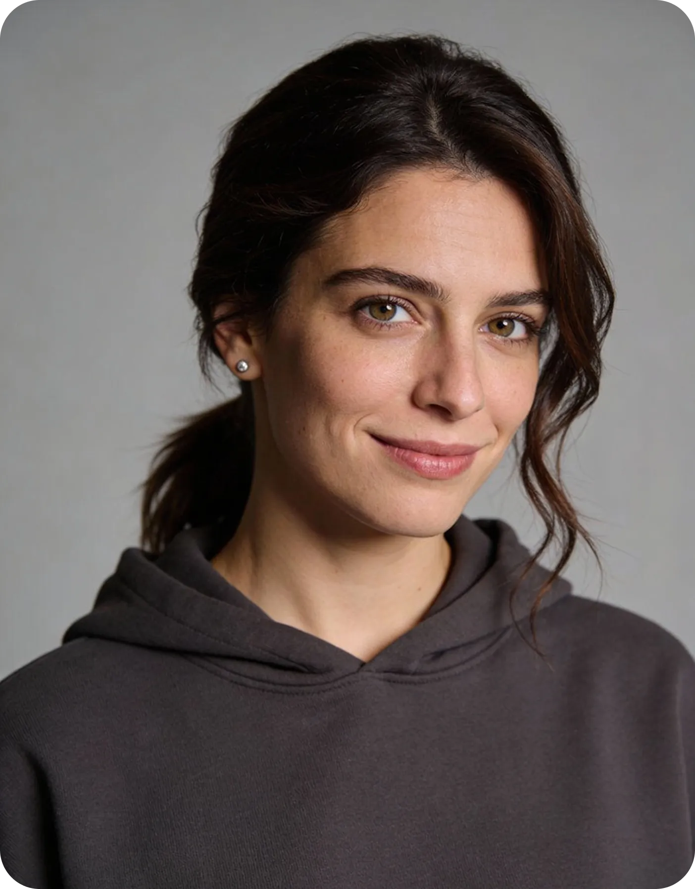 Glimlachende jonge vrouw in een donkere hoodie tegen een grijze achtergrond.